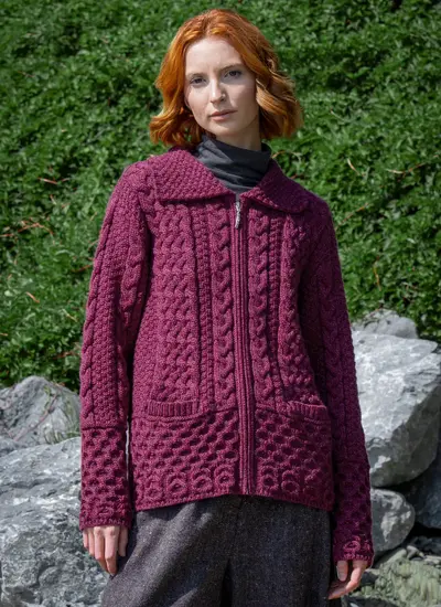 Red head model in front of greenery in grace full zip aran cardigan in raspberry melange